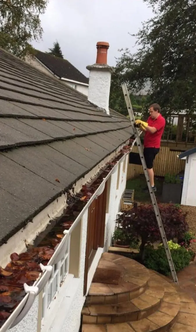 Gutter before clearing, packed with wet leaves, with a cleaner on a ladder