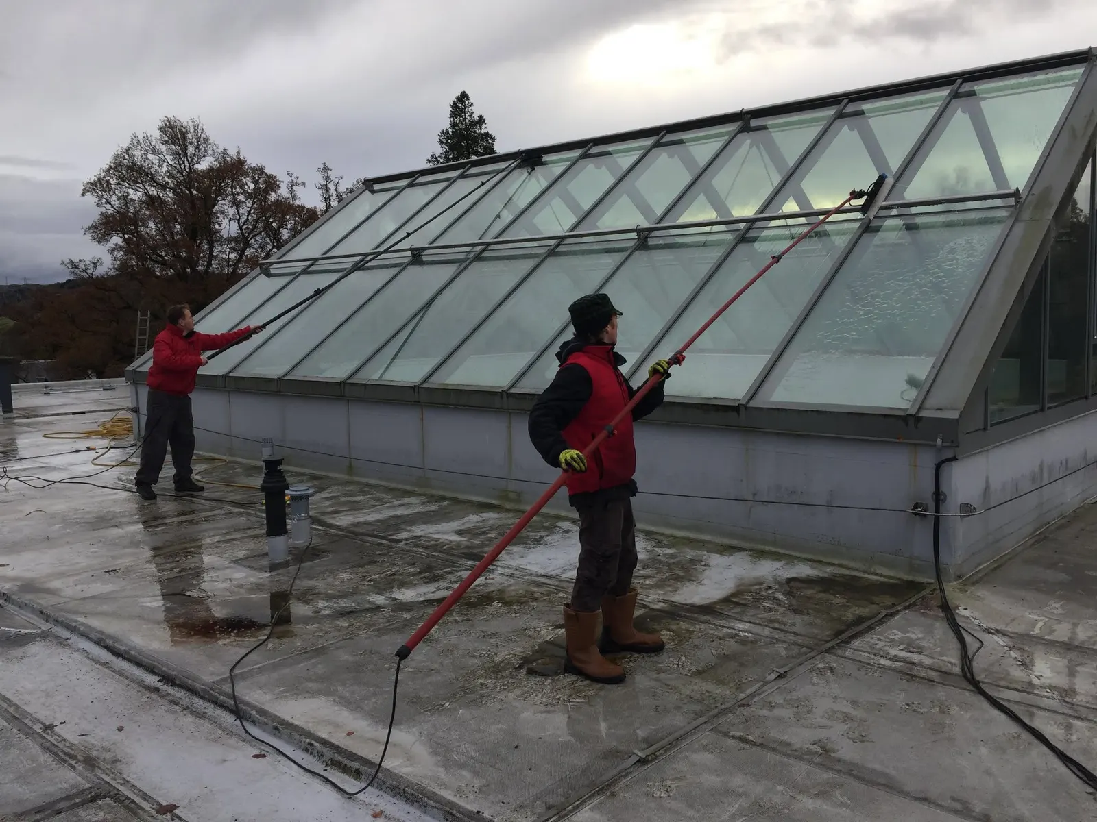Two cleaners washing a large glass roof light from a flat roof